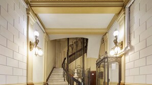 A grand staircase with ornate railings and wall sconces, leading to a landing with a glass door. - Casa Abamita (Barcelona)