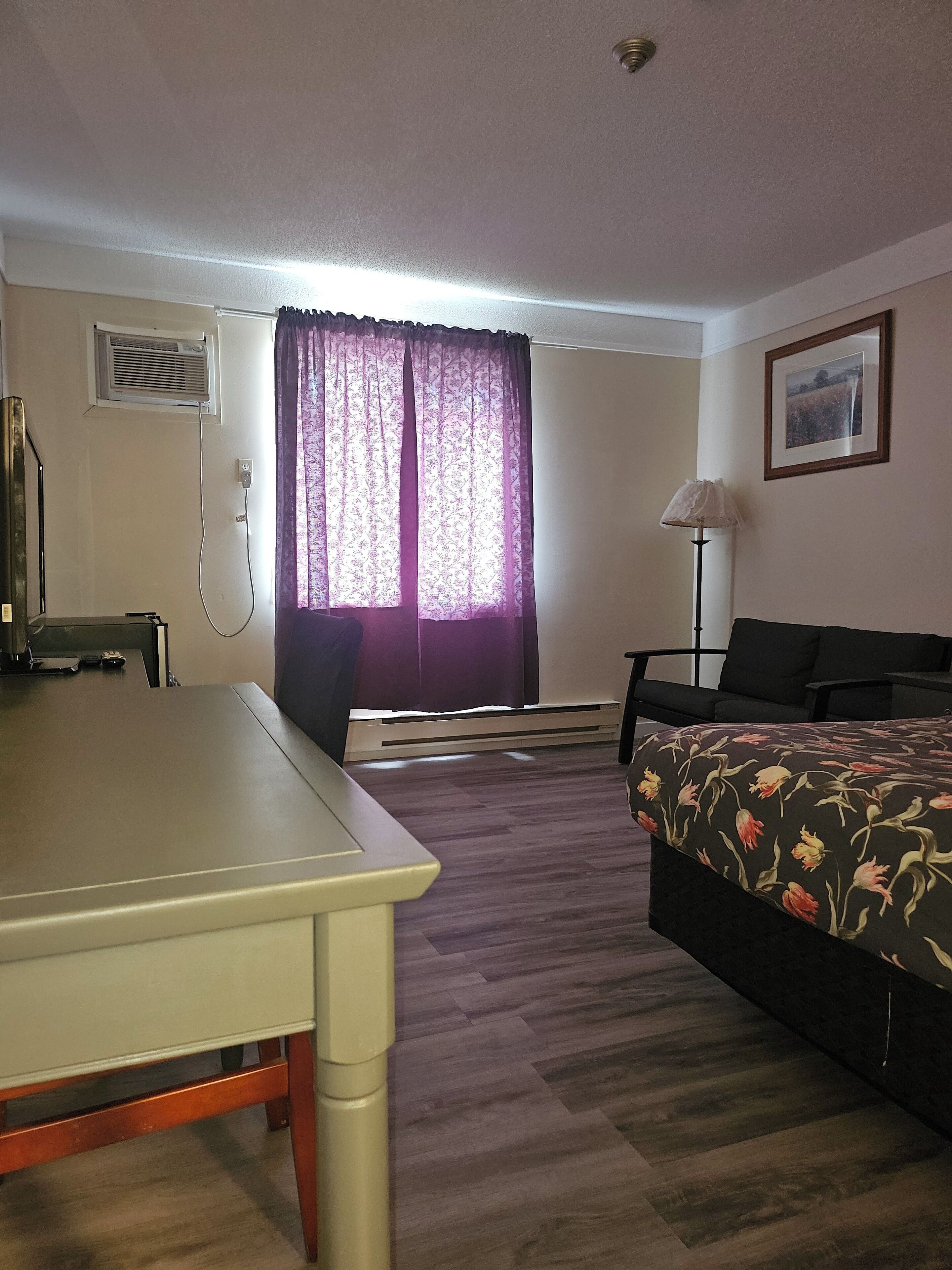 A hotel room with a bed, a desk, a chair, a lamp, and a window with curtains.