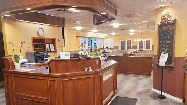 A reception area with a wooden counter, a clock, and a menu board. - Moosomin Country Squire Inn (Moosomin)
