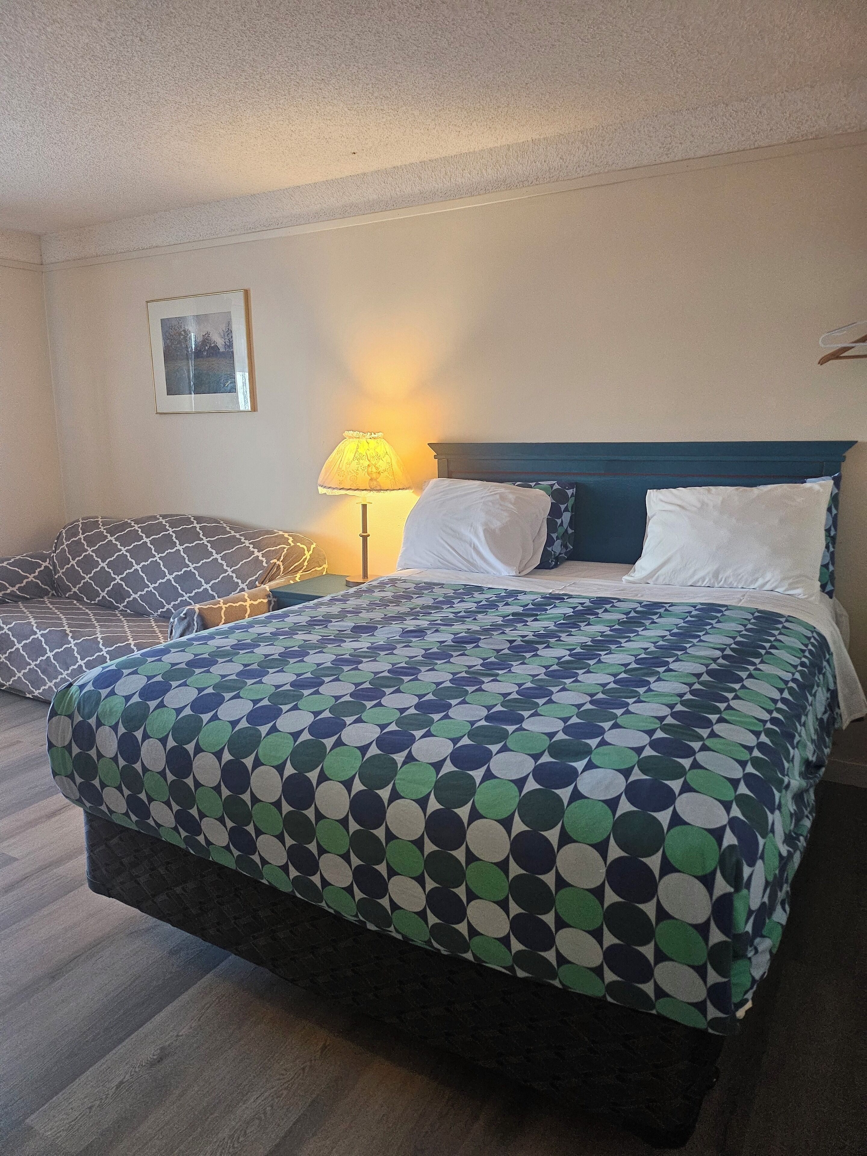 Une chambre d’hôtel avec un lit, une table de chevet, une lampe et un tableau encadré au mur.