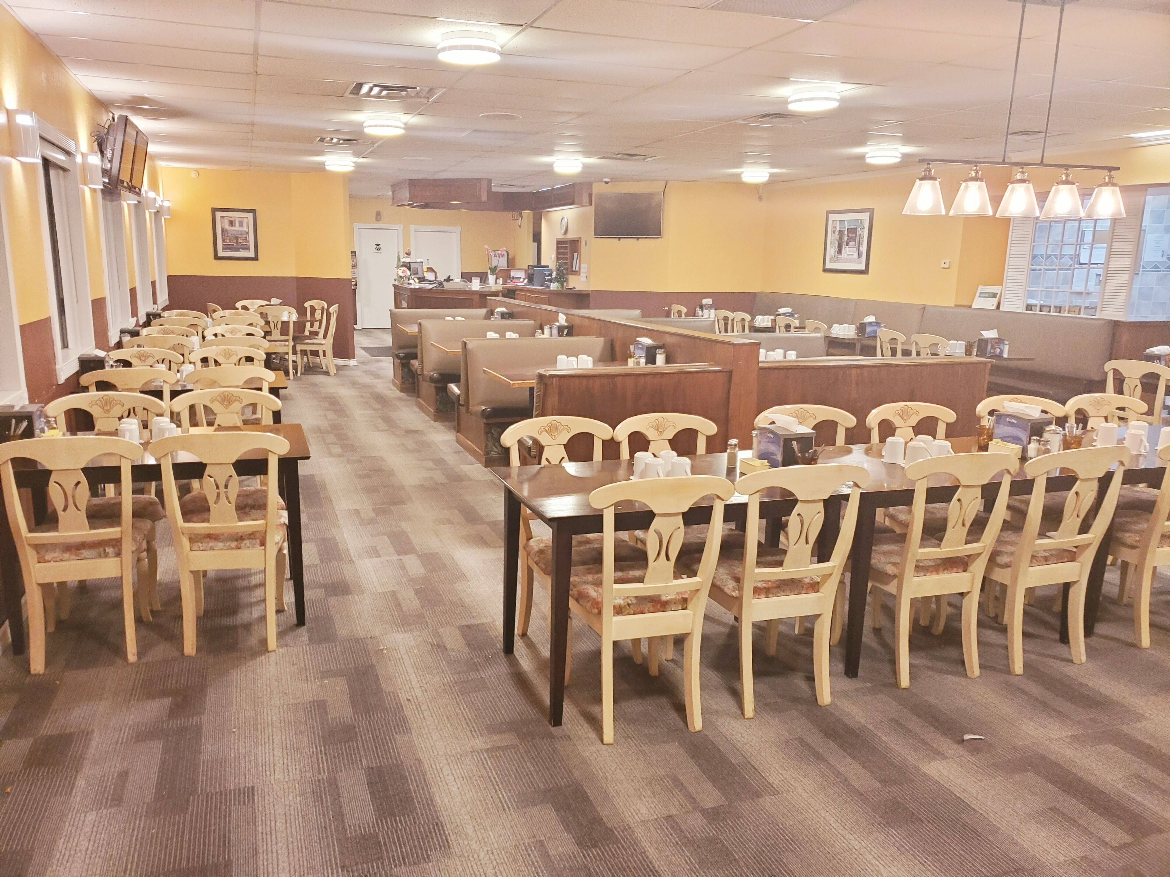 A restaurant with multiple dining tables and chairs, a counter, and a view of the outside through large windows.