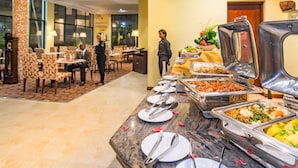 Een buffetopstelling met diverse gerechten, een bedienend personeelslid en een eetgedeelte met tafels en stoelen.