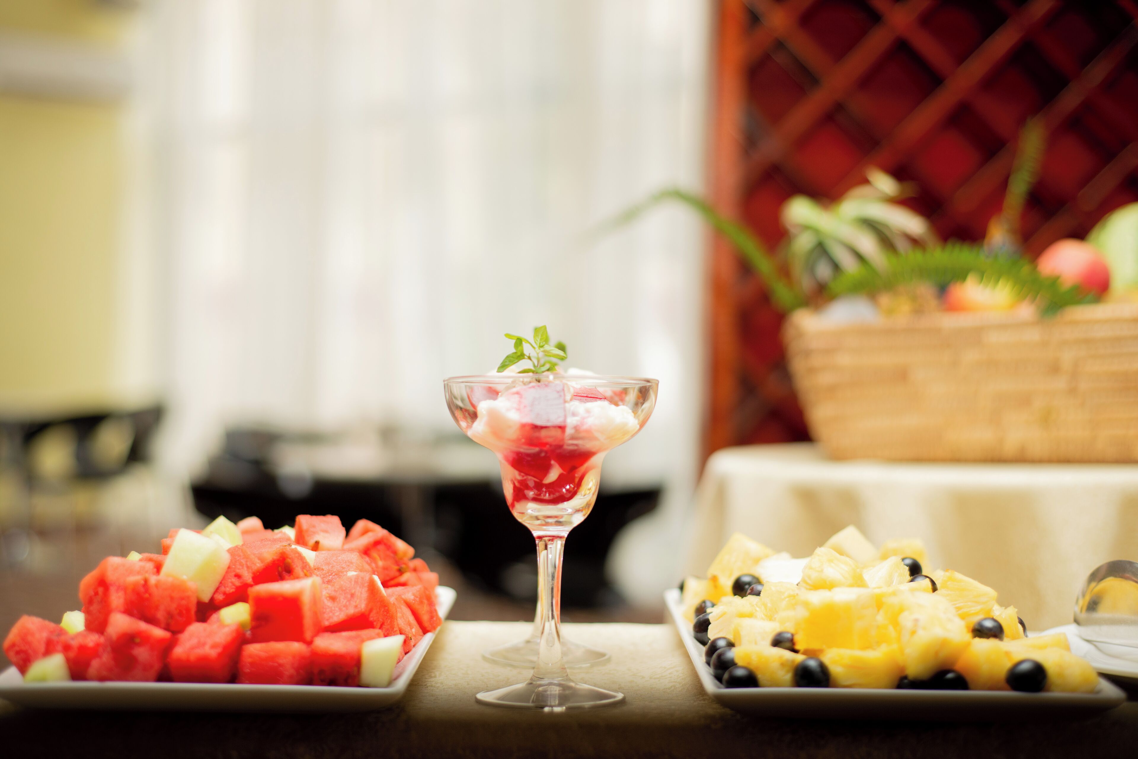 A table with three fruit platters and a glass of fruit cocktail.