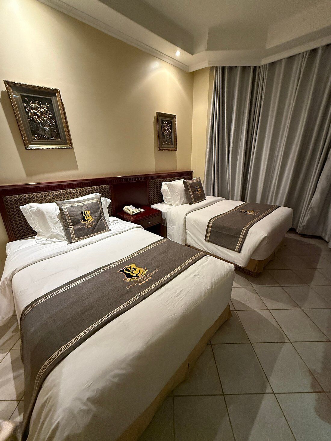 A hotel room with two beds, a nightstand, a telephone, and a large window with curtains.
