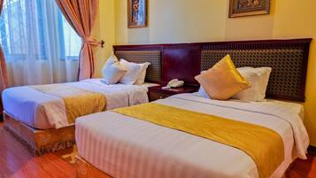Two double beds with matching headboards, a bedside table with a phone, and a window with sheer curtains.