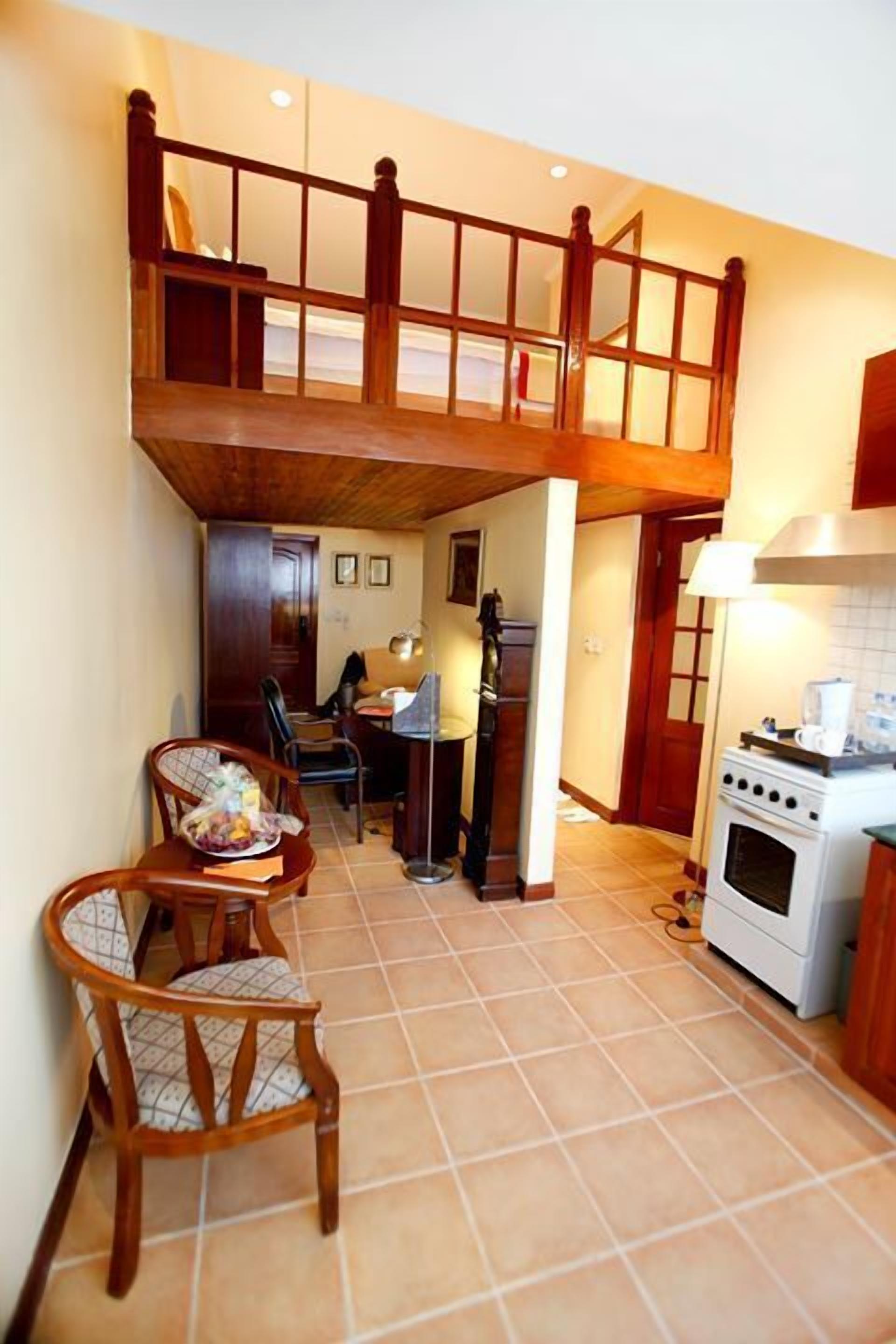 A kitchen with a wooden staircase, a dining area with chairs, and a refrigerator.