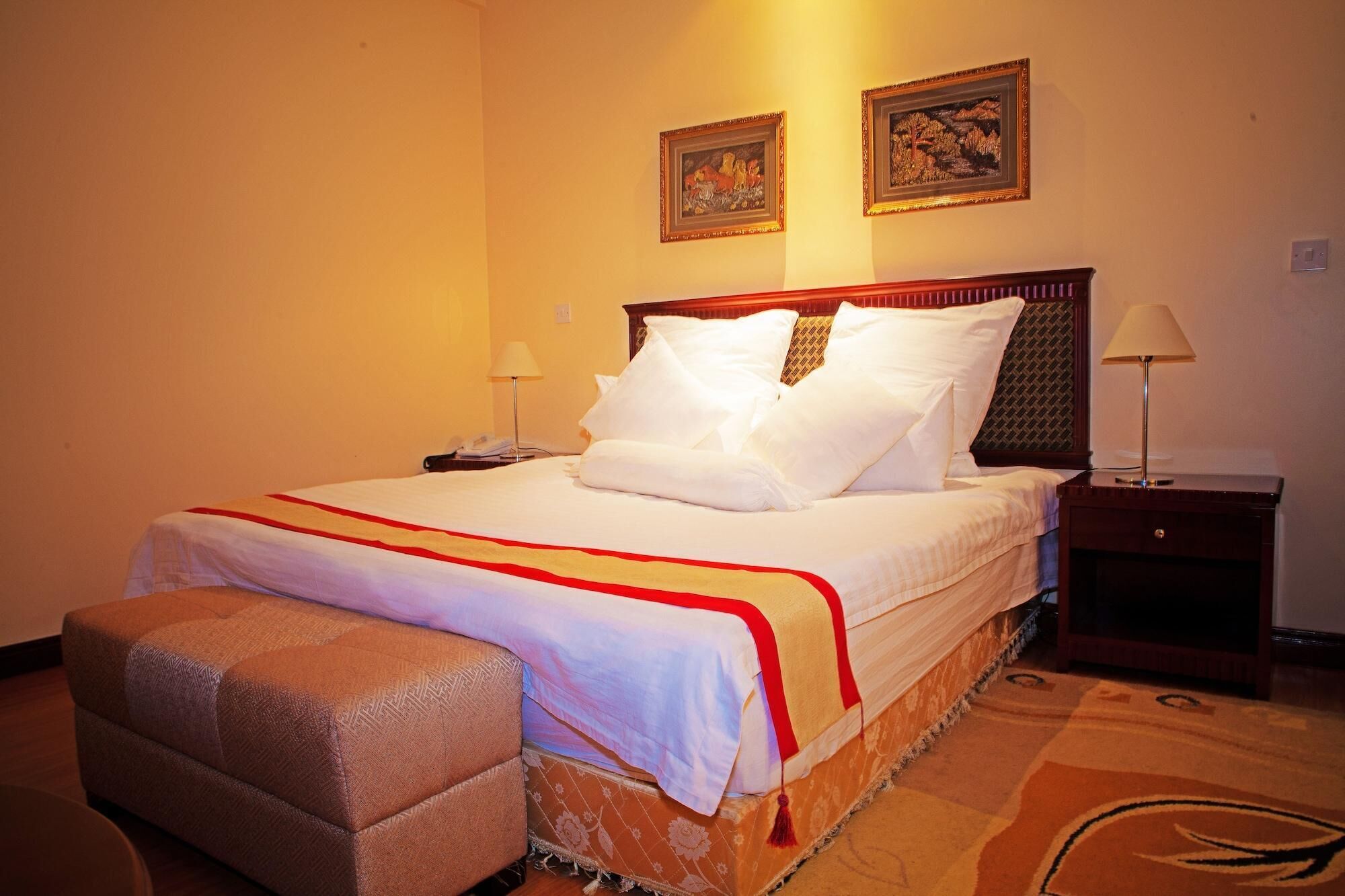 Une chambre d’hôtel avec un lit, des tables de chevet, une lampe et deux tableaux encadrés au mur.