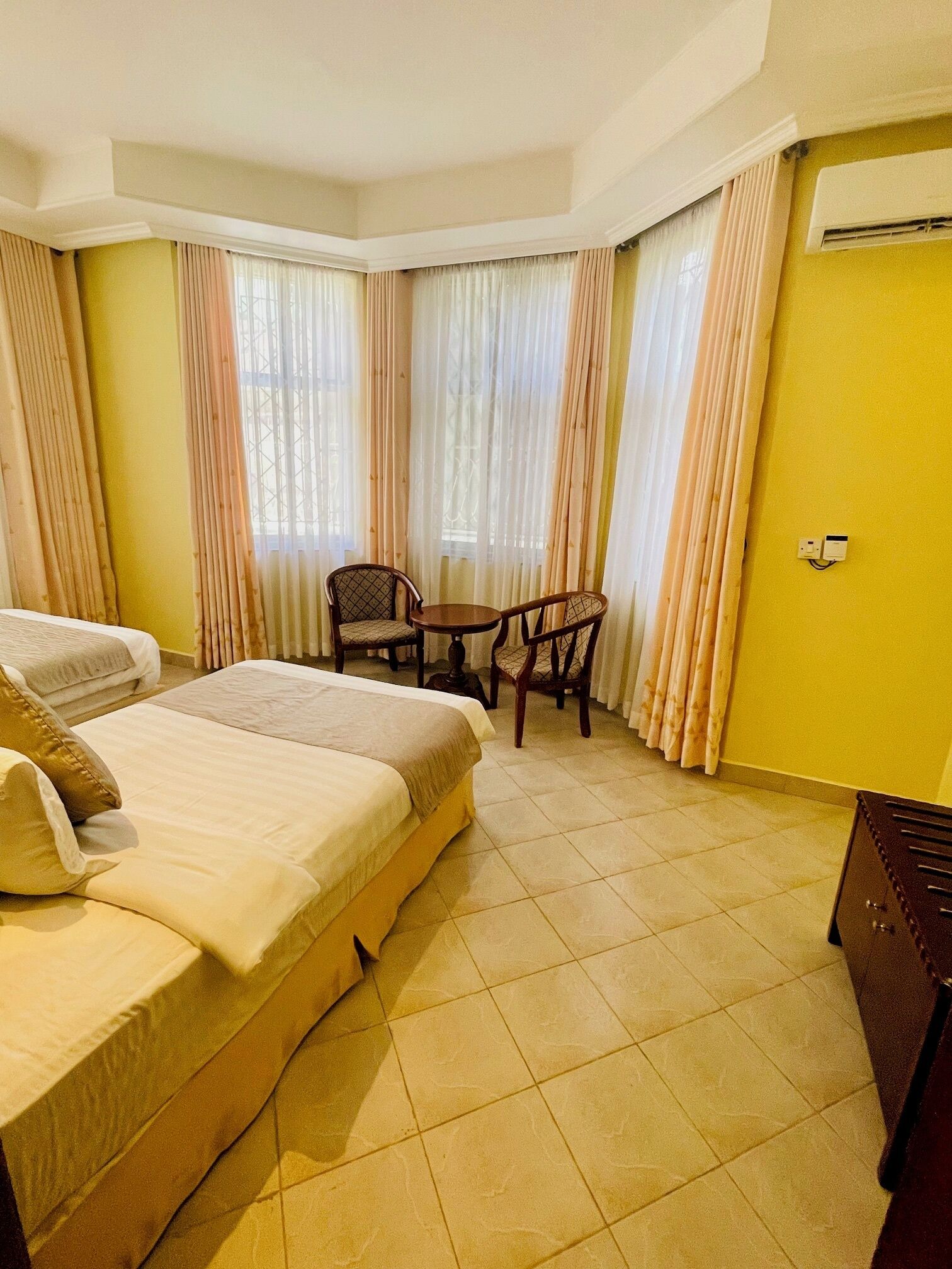 A hotel room with a large bed, a small table with two chairs, and a window with curtains.