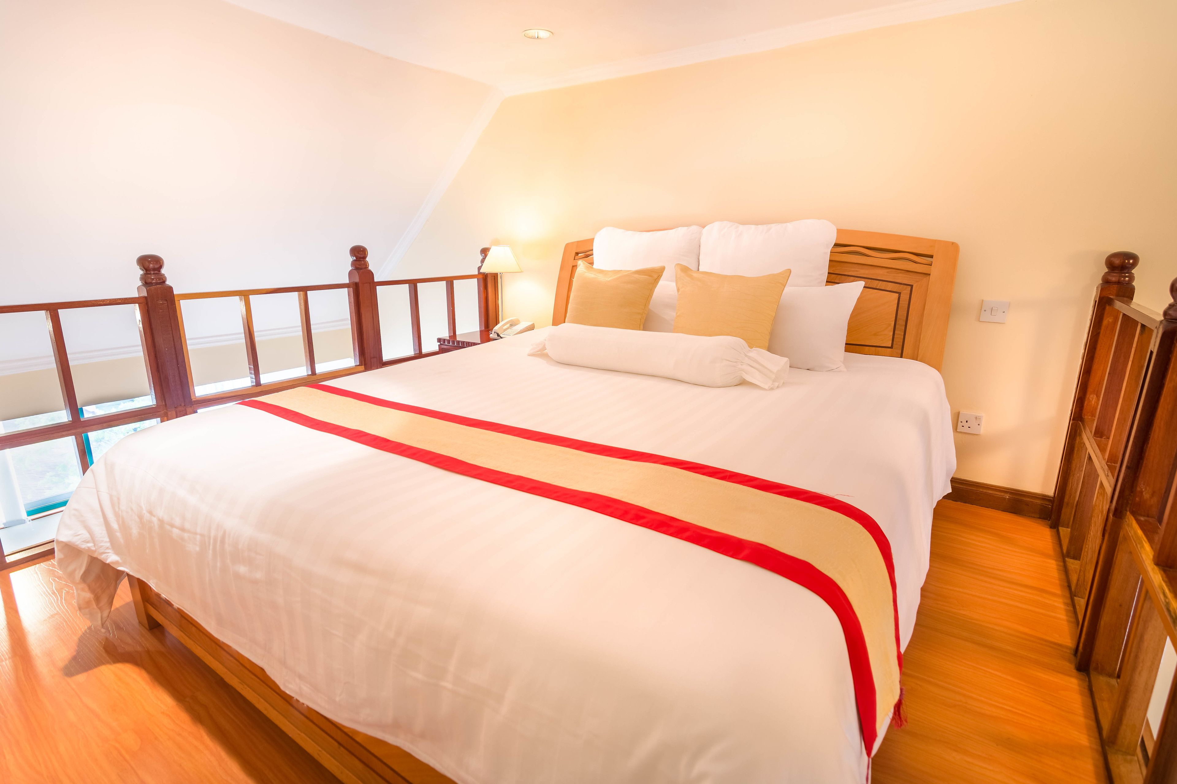 A hotel room with a large bed, wooden headboard, and a balcony with a wooden railing.