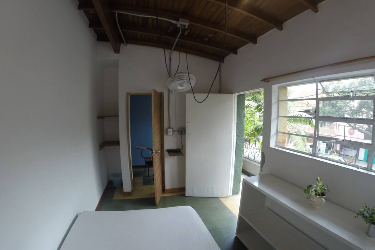 Une pièce avec un lit, une fenêtre donnant sur un beau paysage, un ventilateur de plafond et une porte qui mène à une autre pièce.