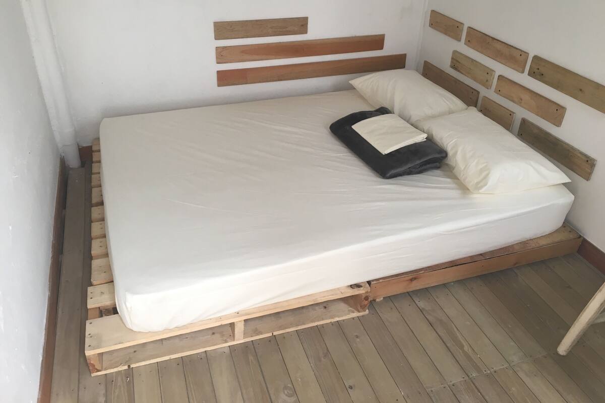Un lit simple avec un cadre et une tête de lit en bois, une literie blanche et une couverture pliée.
