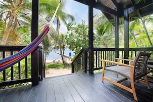 Um deck de madeira com rede e mobiliário de vime, com vista para uma praia e palmeiras.