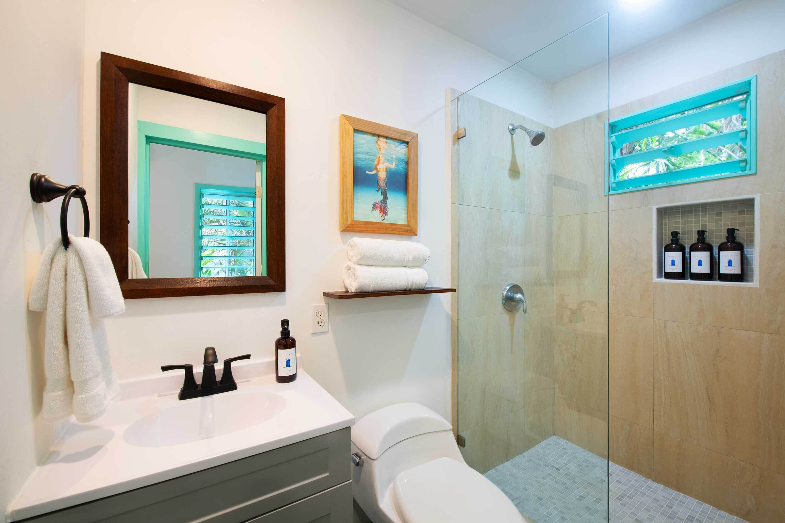 A modern bathroom with a glass-enclosed shower, a white sink with a mirror above it, and a framed picture on the wall.