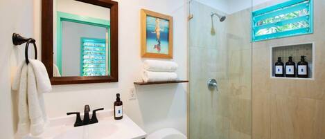 A modern bathroom with a glass-enclosed shower, a white sink with a mirror above it, and a framed picture on the wall.