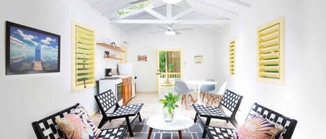 A room with a ceiling fan, a table with chairs, a plant, and a painting on the wall.