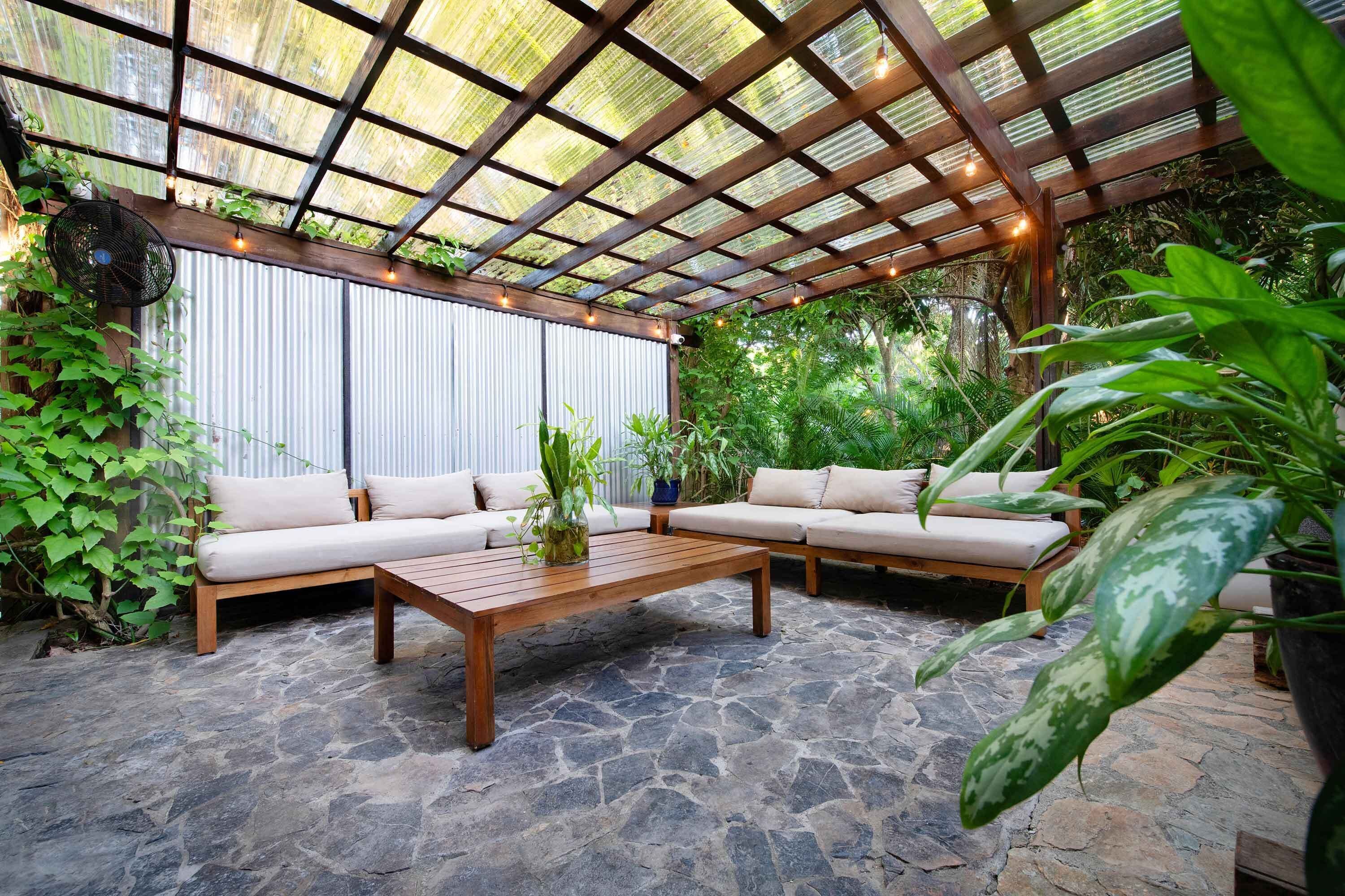 Un patio al aire libre con una mesa de madera, dos sofás color beige y piso de piedra.