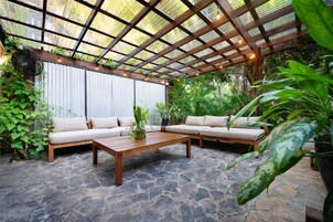 Un patio al aire libre con una mesa de madera, dos sofás color beige y piso de piedra.