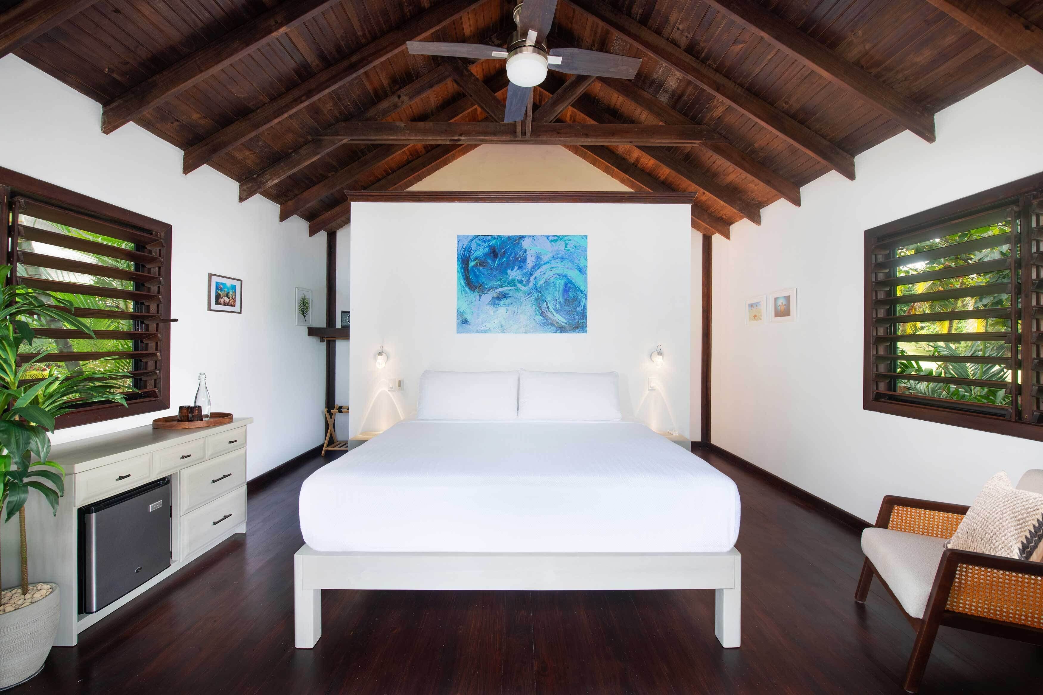Ein Schlafzimmer mit einem großen Bett, Holzbalkendecke, Deckenventilator und einem Fenster mit Jalousien.