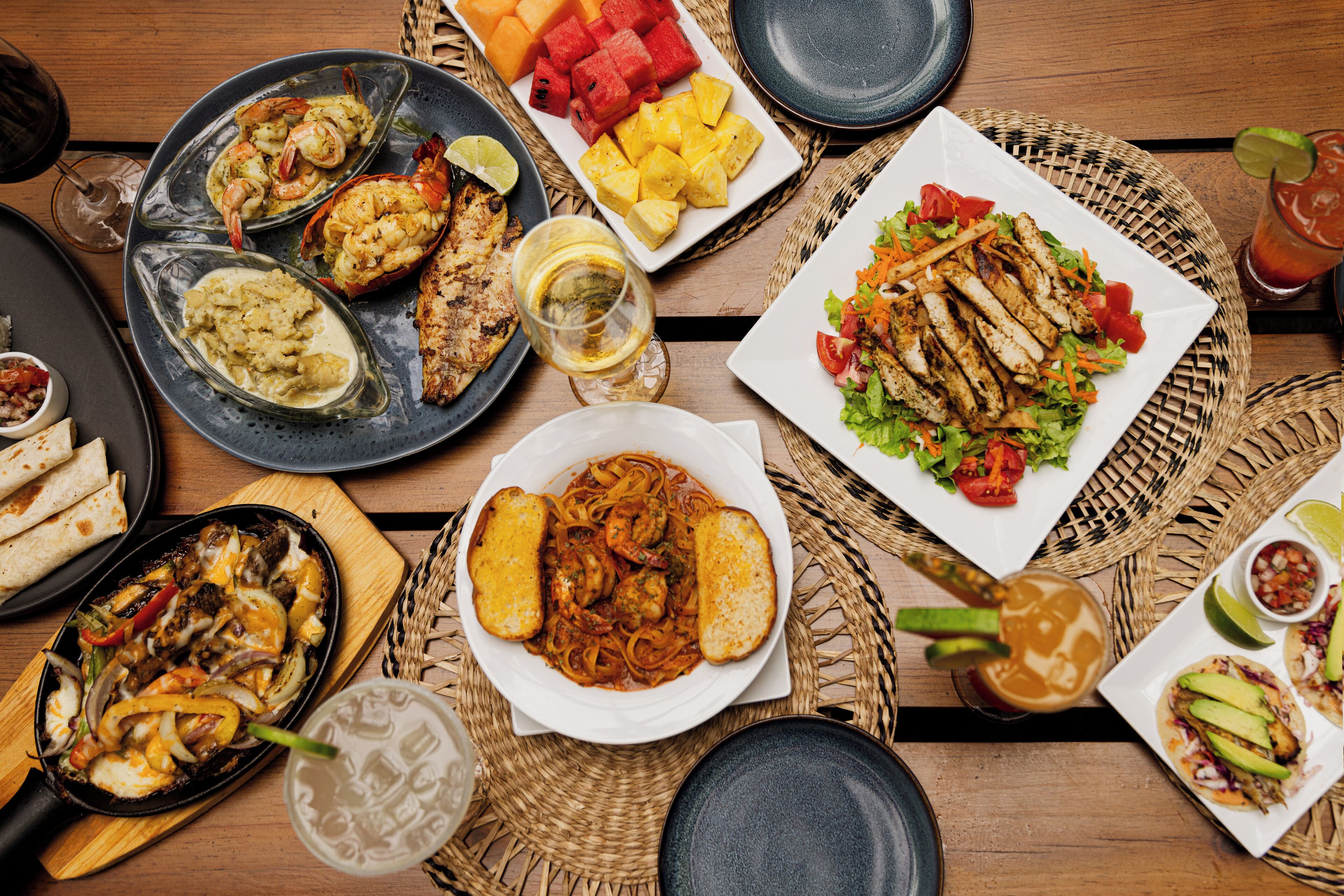 A variety of dishes on a wooden table, including seafood, grilled chicken, and salads.