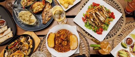 A variety of dishes on a wooden table, including seafood, grilled chicken, and salads.