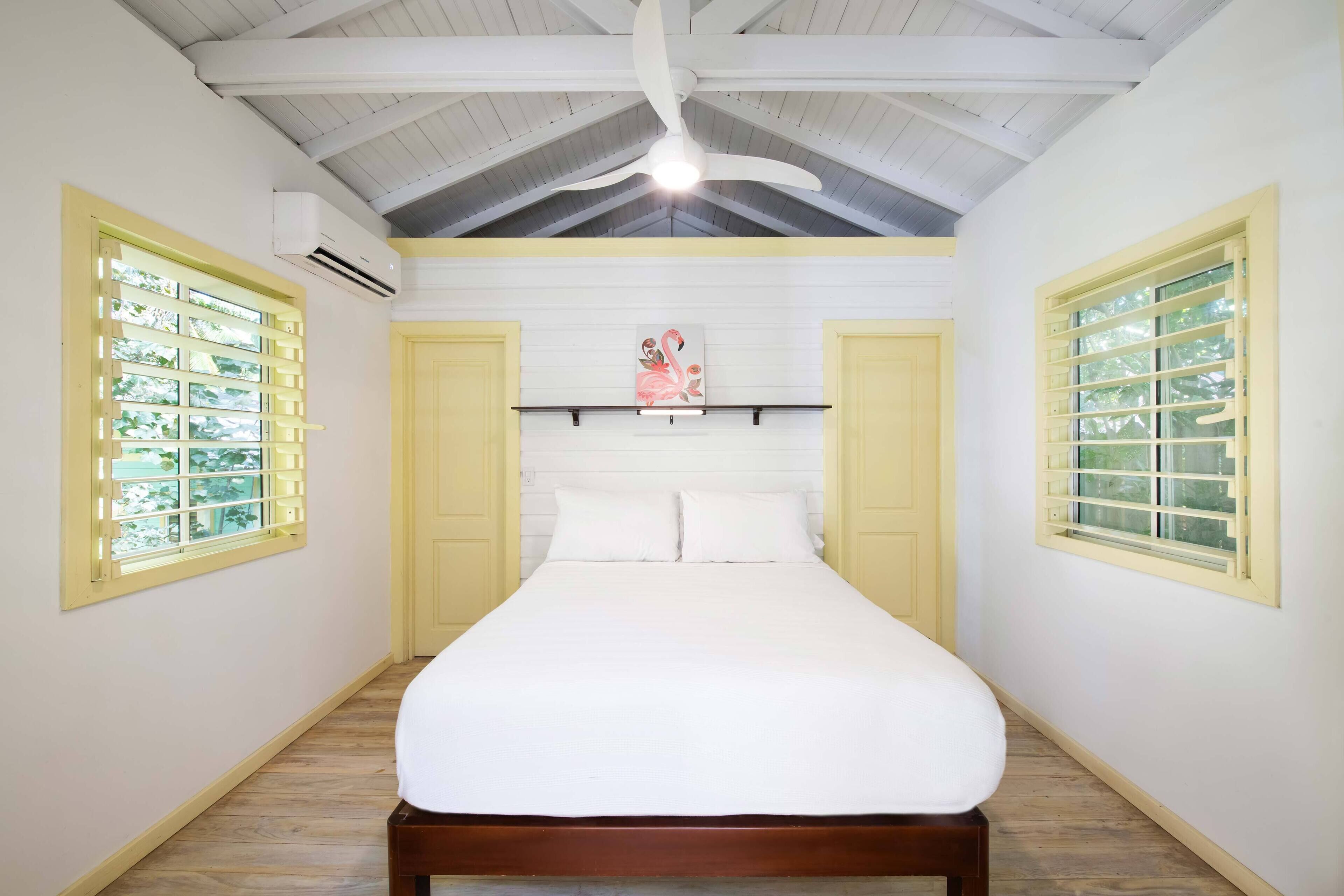 Une chambre à coucher avec un lit, un ventilateur de plafond et une fenêtre donnant sur un paysage verdoyant.