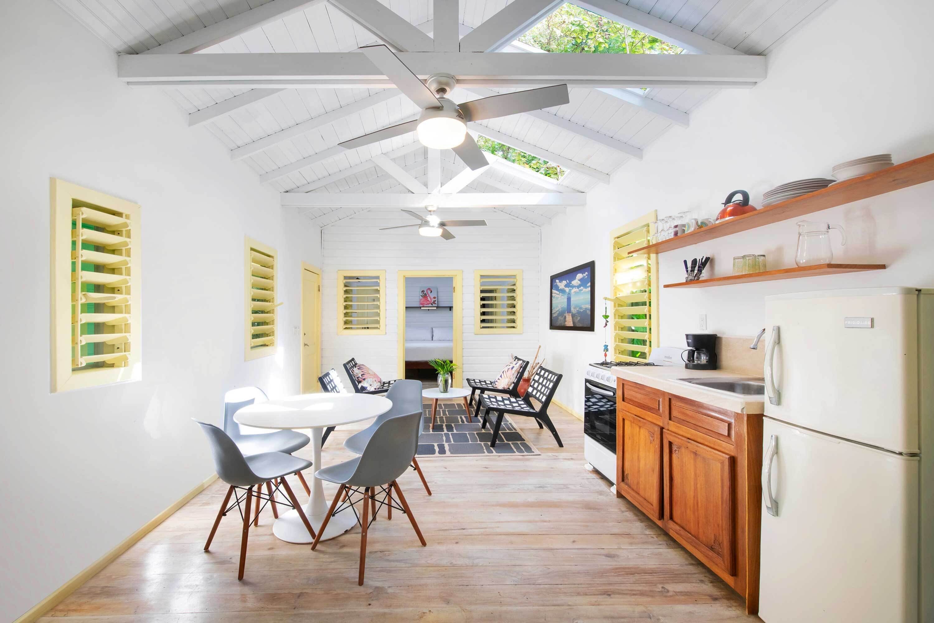A modern kitchen with wooden cabinets, a white refrigerator, and a dining area with a white table and grey chairs.