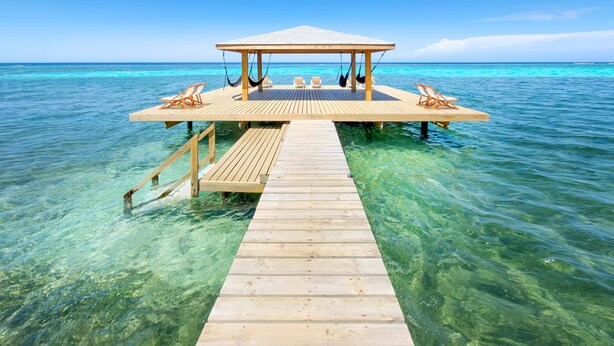 Une jetée en bois mène à un belvédère doté d’un toit, le tout étant entouré d’une eau turquoise.