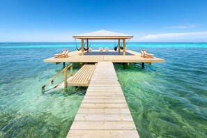 Una banchina di legno conduce a un gazebo con tetto, immerso in acque turchesi.