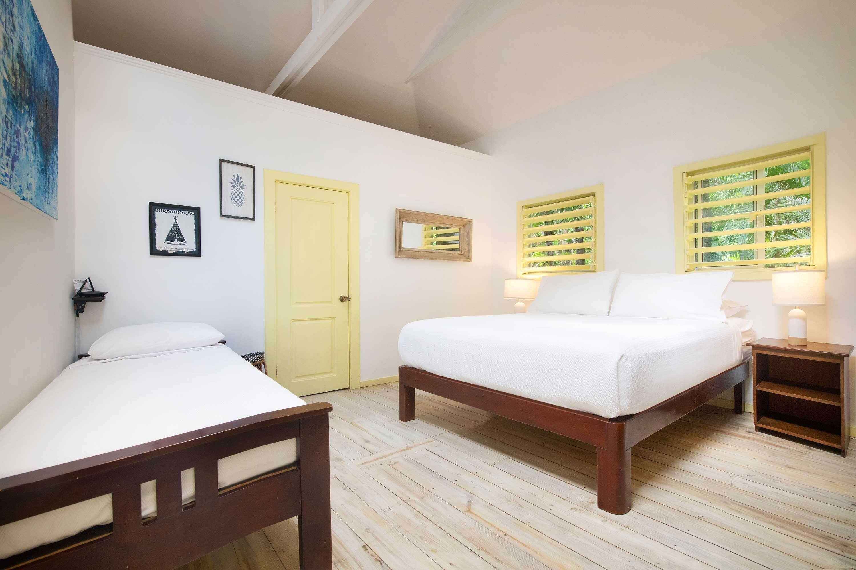 A bedroom with a bed, a bedside table, a nightstand, a door, and a window with shutters.