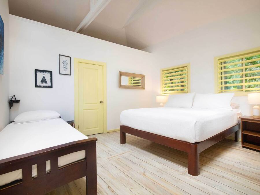 A bedroom with a bed, a bedside table, a nightstand, a door, and a window with shutters.
