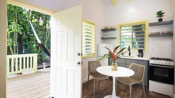 Una cocina con comedor, una puerta blanca que da a un balcón y vistas al exterior con vegetación.