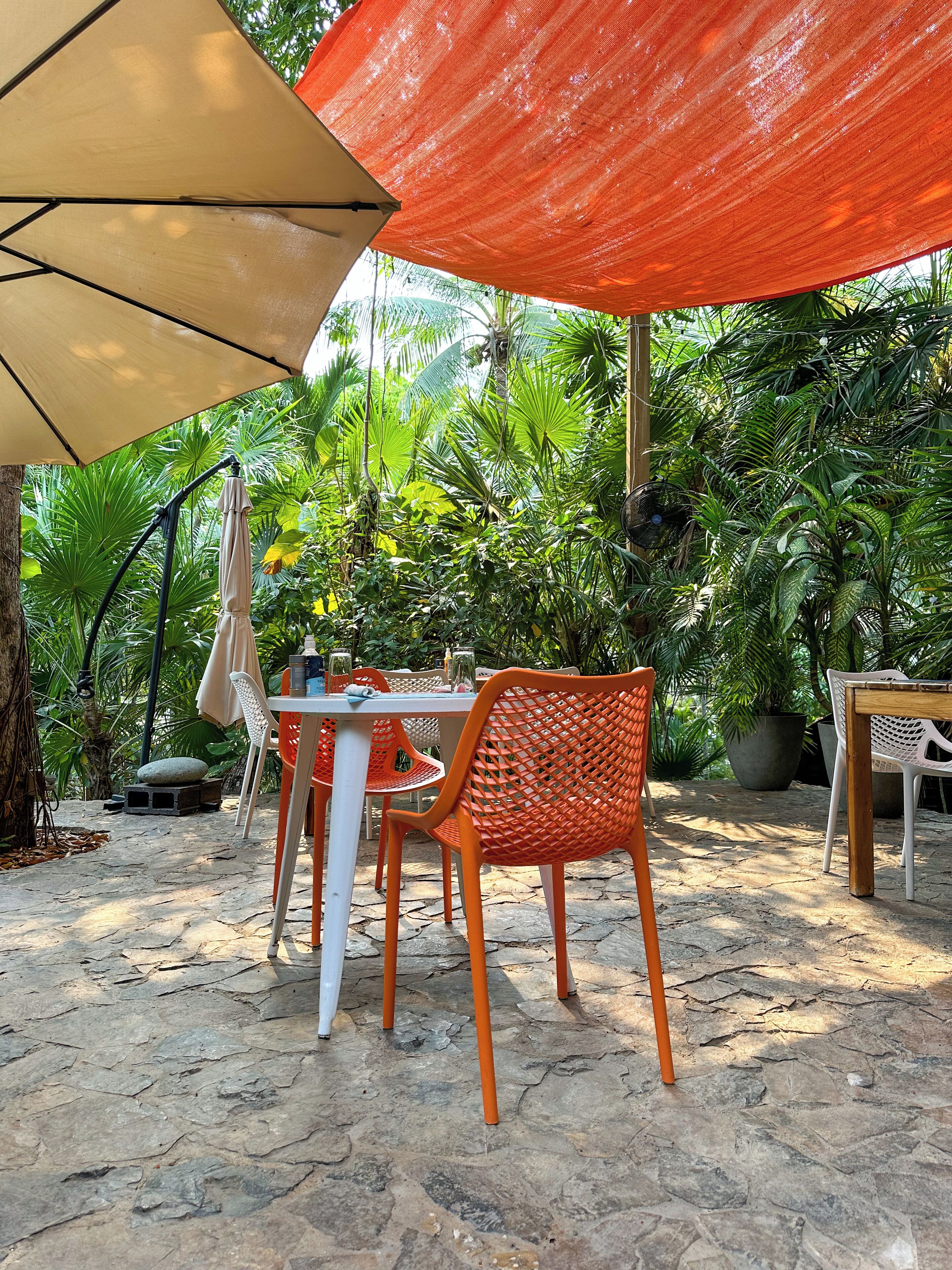Un patio al aire libre con suelo de piedra, una mesa, sillas y una gran sombrilla que da sombra.