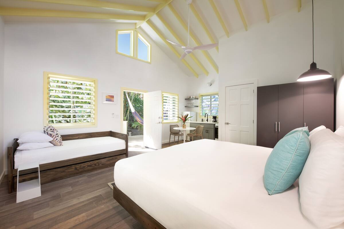 A bedroom with two beds, a desk, and a kitchenette.