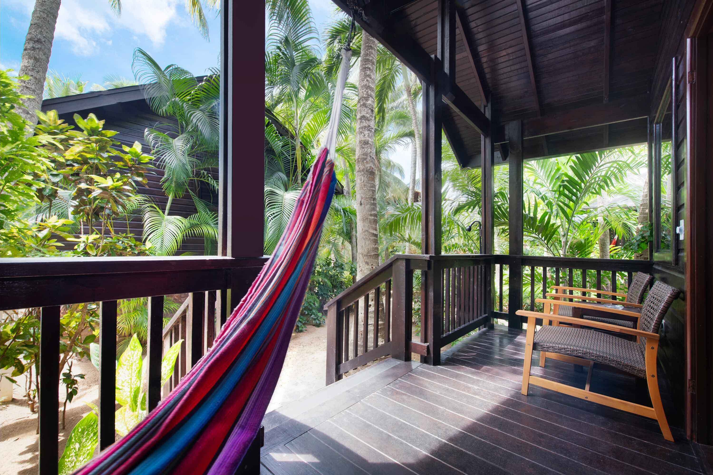 A wooden deck with a hammock, wooden chairs, and a view of palm trees.