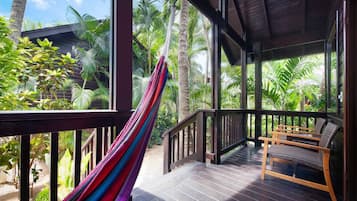 A wooden deck with a hammock, wooden chairs, and a view of palm trees.