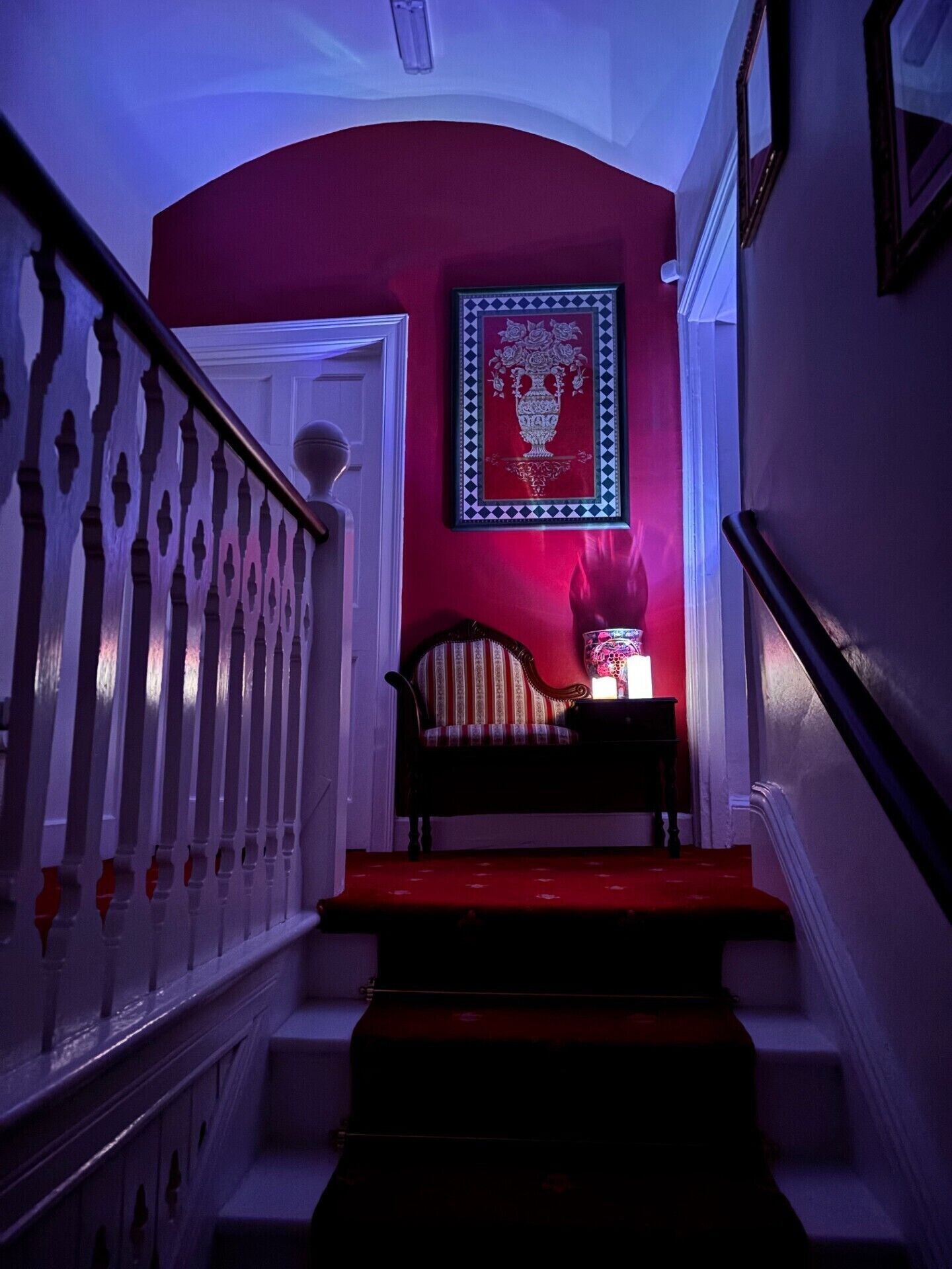 Una escalera con una pared roja, una obra de arte enmarcada y una lámpara de mesa encendida.