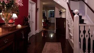 A wooden staircase with white balusters leading to a second floor. A dark wooden floor extends through the hallway, and a rug is placed at the bottom.