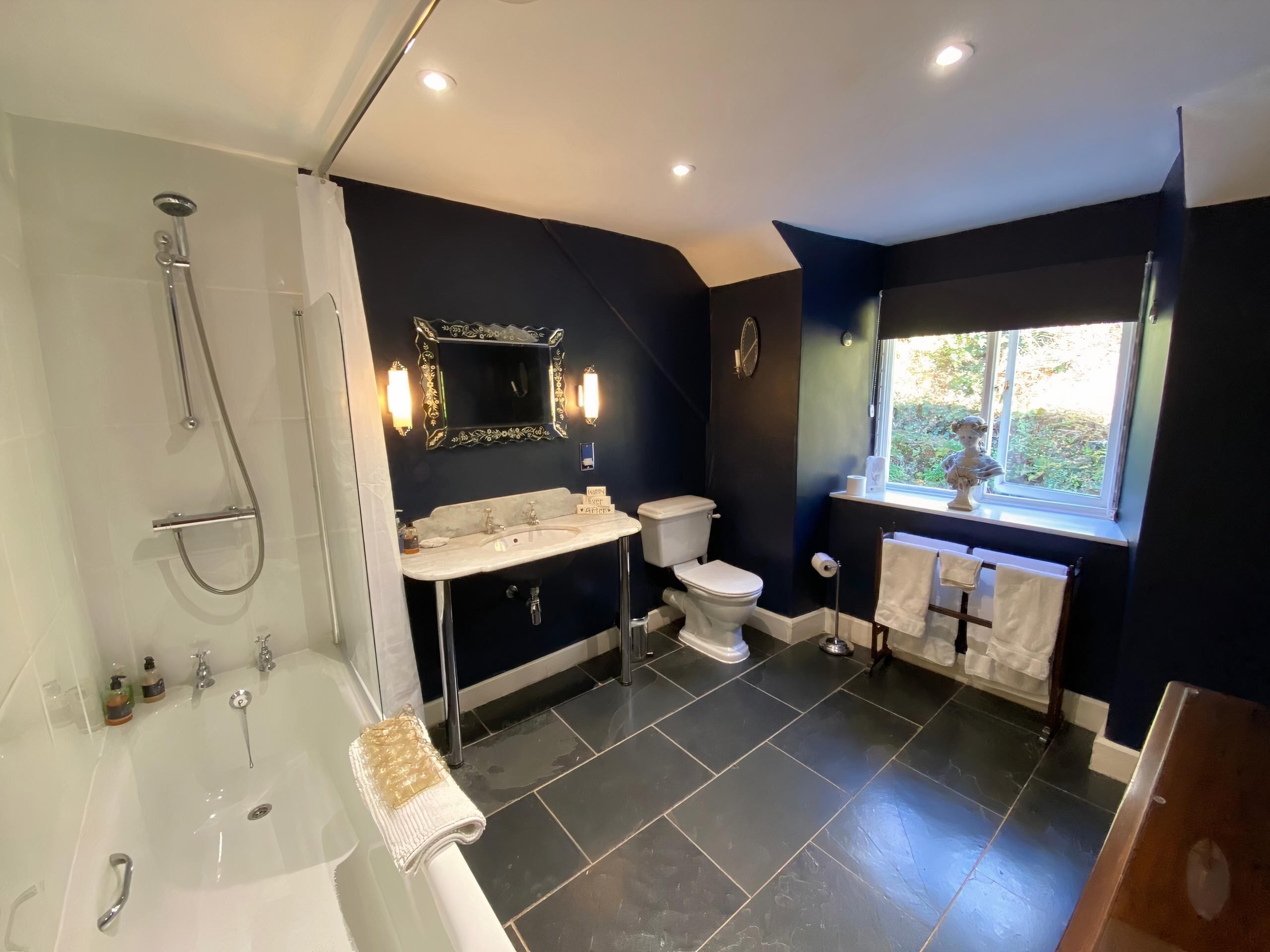 Ein modernes Badezimmer mit einer Badewanne, einem Waschbecken und einer Toilette. Ein Fenster sorgt für natürliches Licht, und über dem Waschbecken befindet sich ein dekorativer Spiegel.