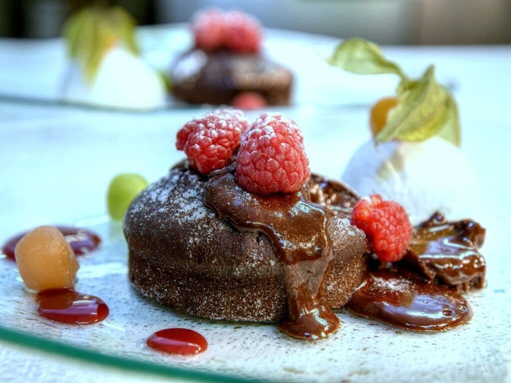 Un postre con salsa de chocolate y frambuesas sobre un plato.