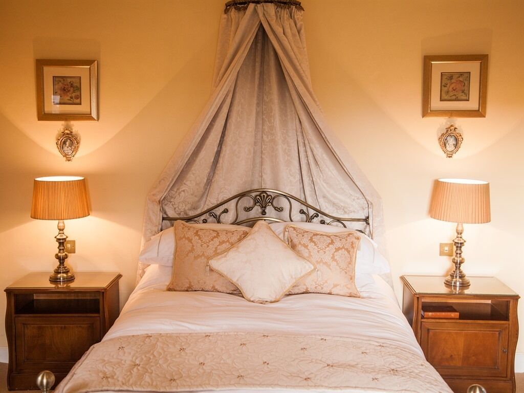 A bedroom with a canopy bed, two bedside tables with lamps, and framed pictures on the walls.