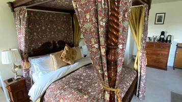 A four-poster canopy bed with floral bedding, a wooden nightstand with a lamp, and a dresser with a mirror.