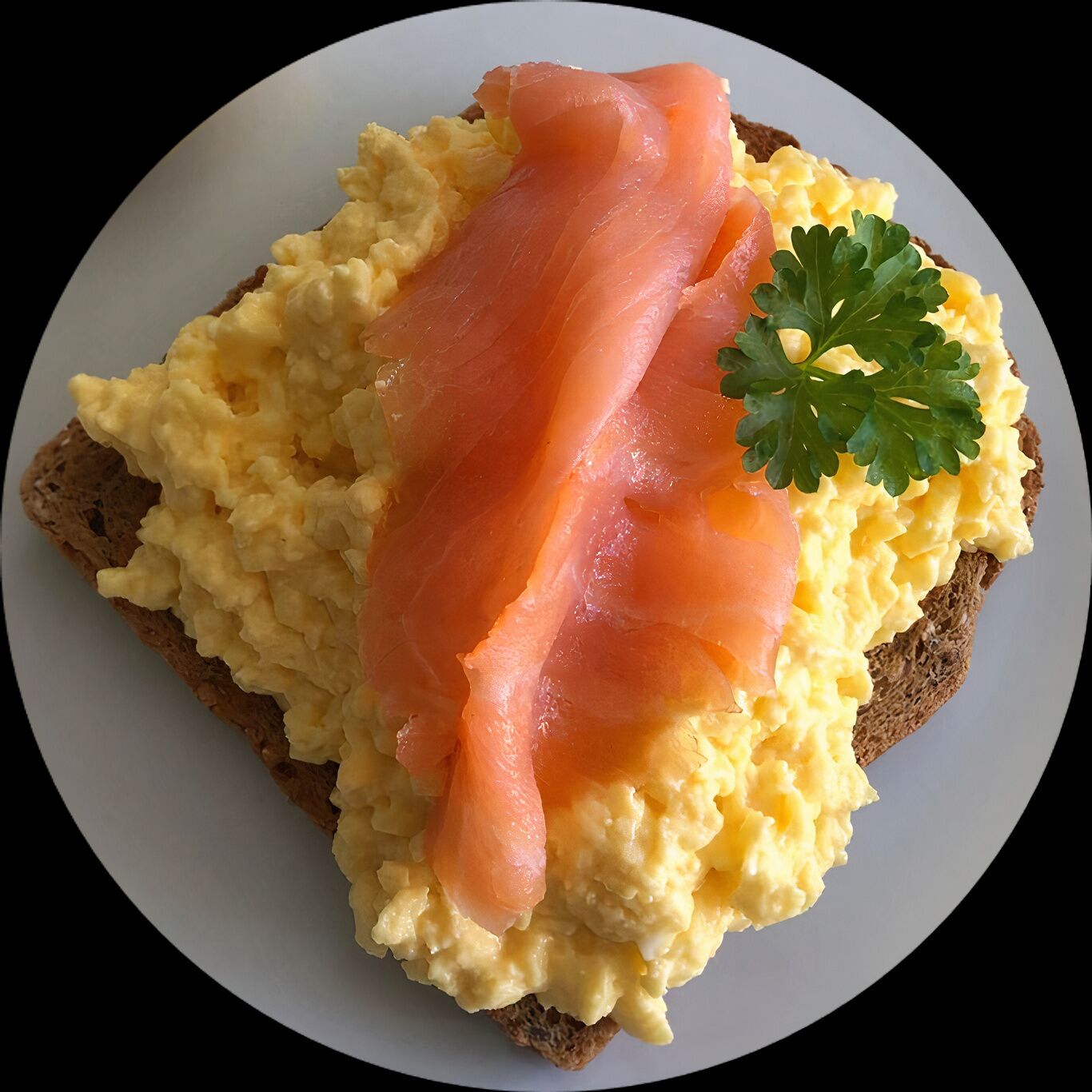 Eine Scheibe Toast mit Rührei und Räucherlachs, garniert mit Petersilie.
