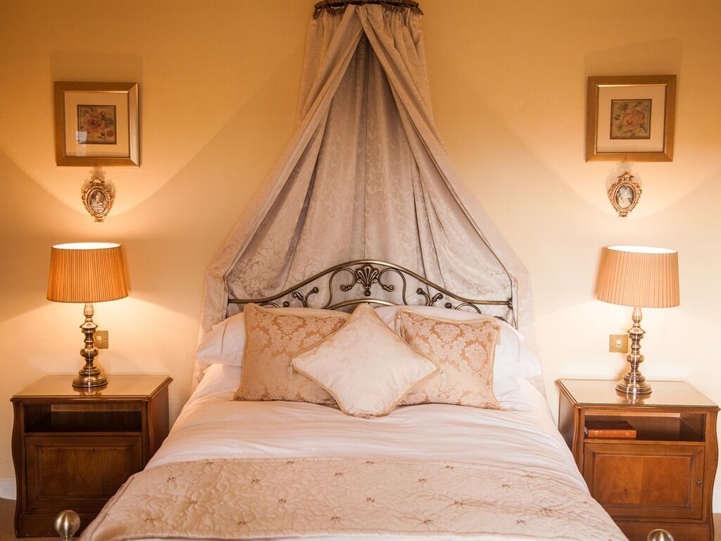 A bedroom with a canopy bed, two bedside tables with lamps, and framed pictures on the walls.