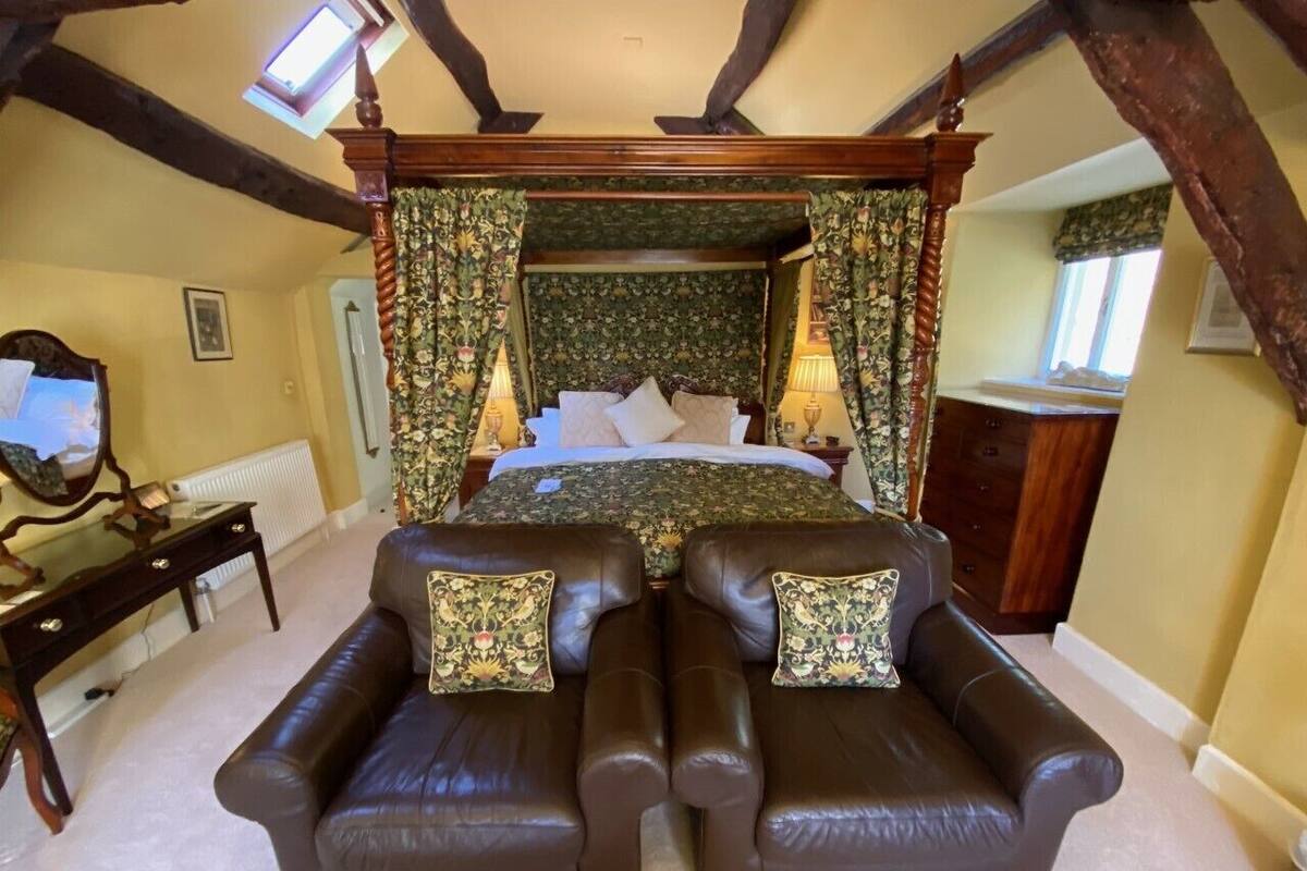 Ein Schlafzimmer mit einem Himmelbett, zwei Ledersesseln, einem Holztisch und einem Spiegel.
