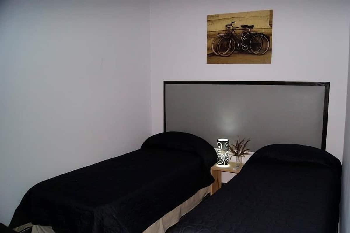 A small room with two single beds, a wooden nightstand with a lamp, and a wall-mounted picture of a bicycle.