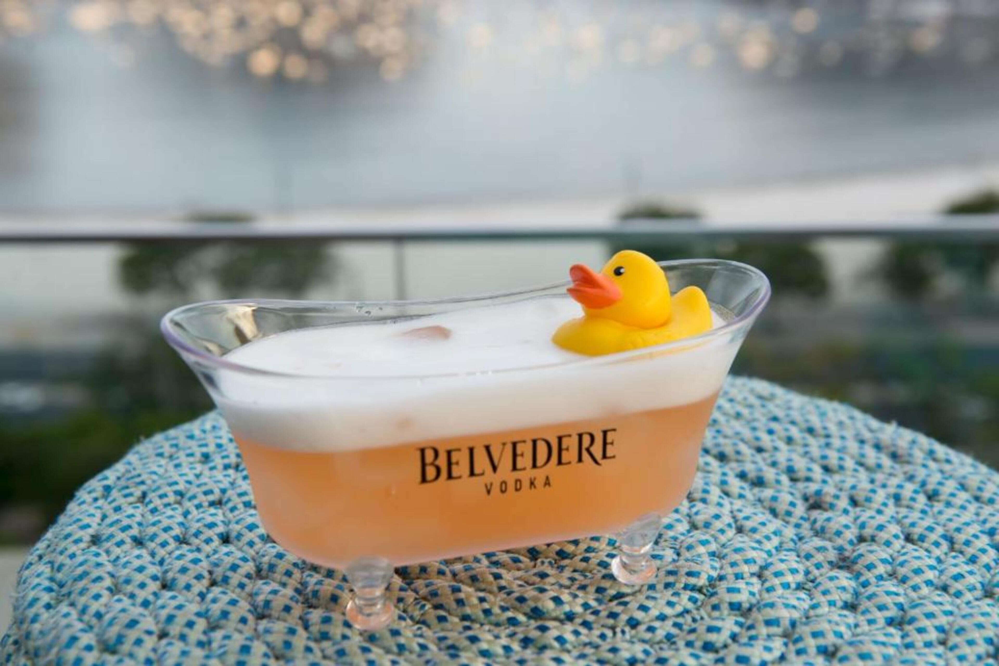 A Belvedere Vodka cocktail with a rubber duck in a clear glass on a blue woven coaster.