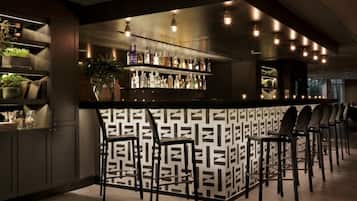 Uma área de bar com parede estampada, prateleiras com garrafas e banquetas.