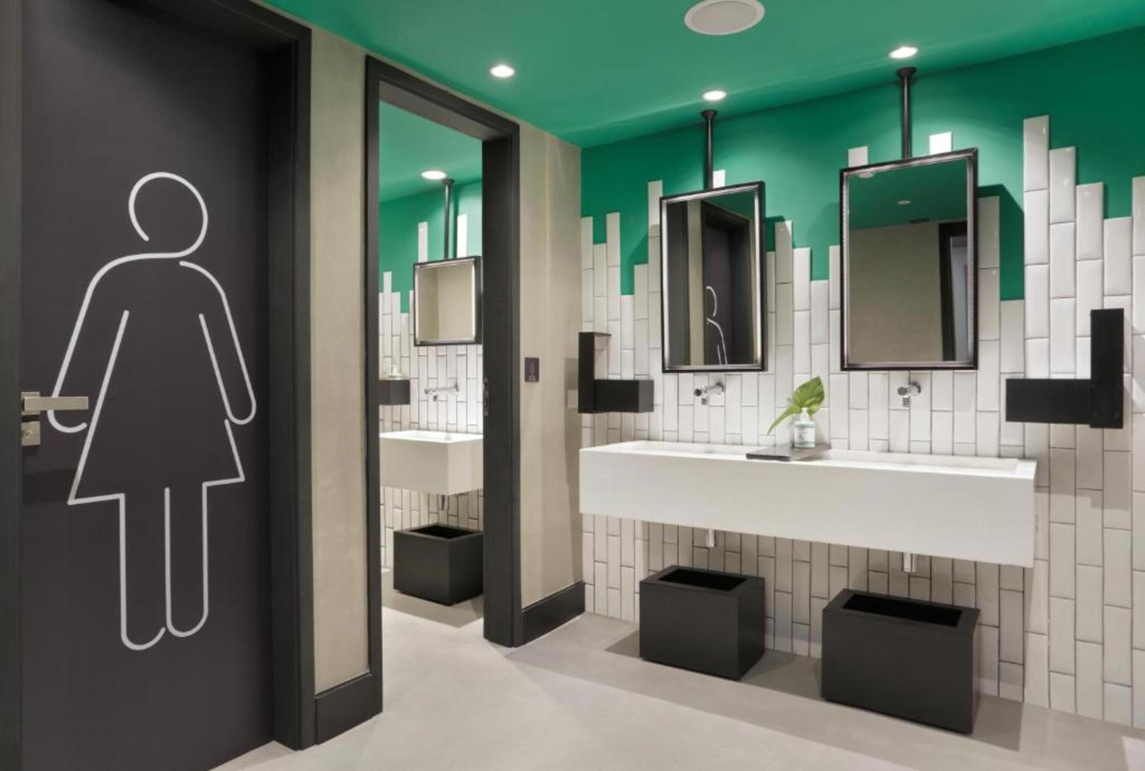 Un baño moderno con un lavamanos blanco, botes de basura negros y una pared de acento verde.