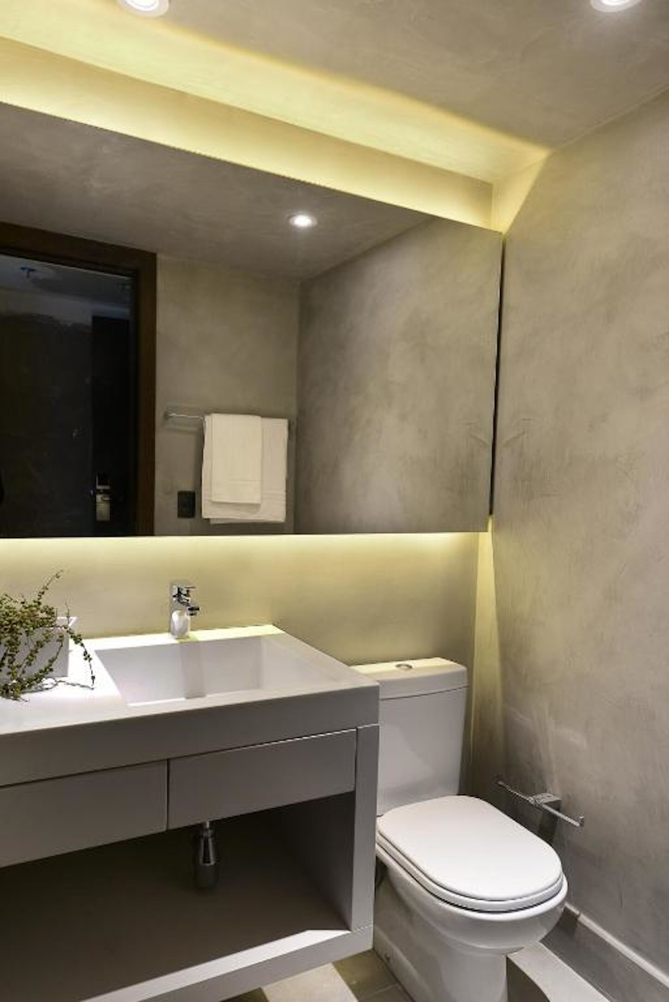Un baño moderno con un espejo grande, un lavabo blanco y un inodoro.