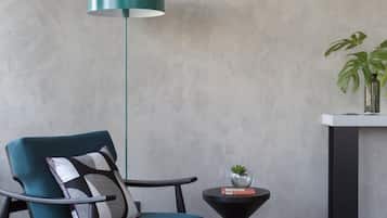 A modern room with a teal chair, a black and white rug, a round black table with a plant, and a teal pendant light.